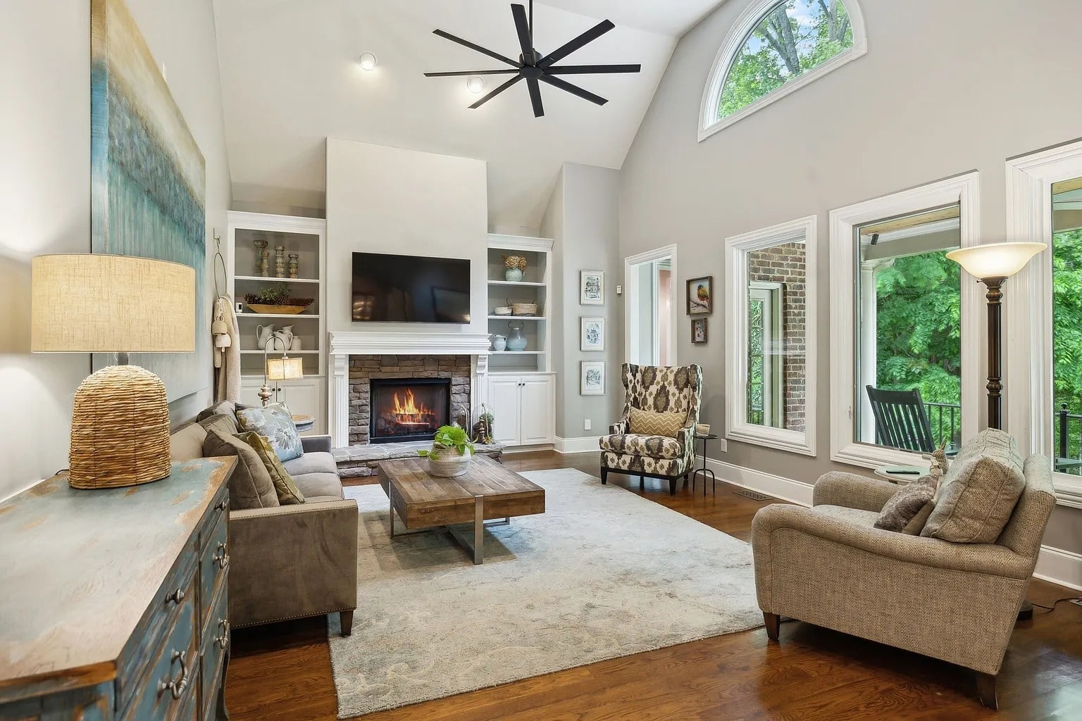 Spacious living room with modern furniture, fireplace, large windows, and a ceiling fan.