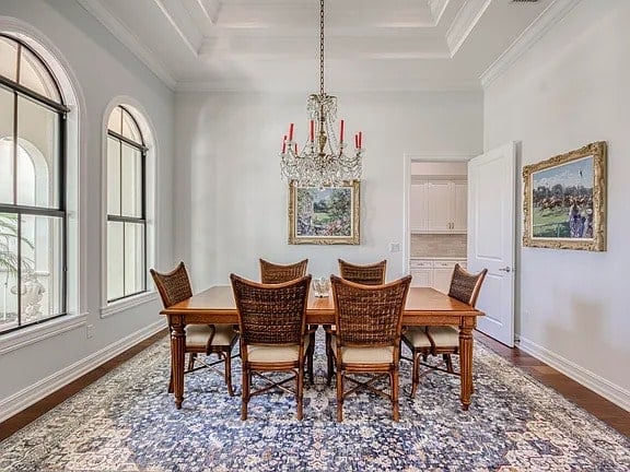 Elegant dining room with a wooden table, wicker chairs, chandelier, and large arched windows.