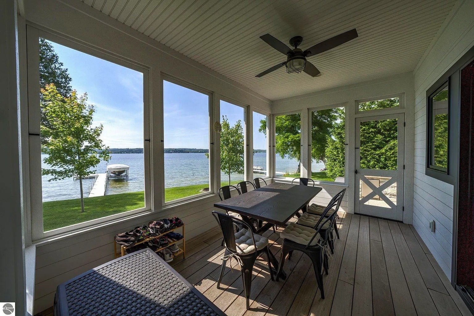 Enclosed porch with dining table, overlooking a lake with a dock and trees outside.