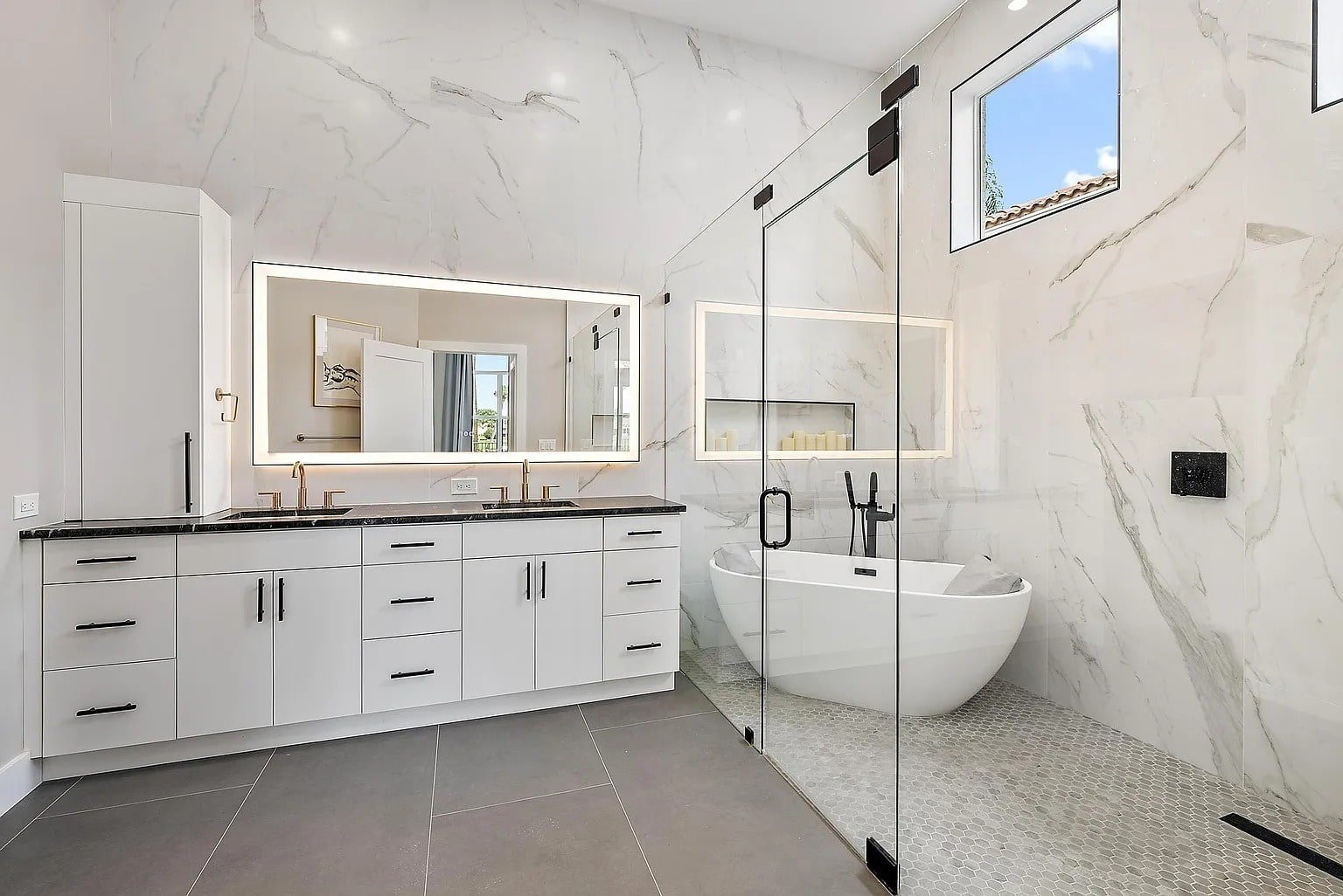 Modern bathroom with white marble walls, black fixtures, freestanding tub, and large mirror with lighting.