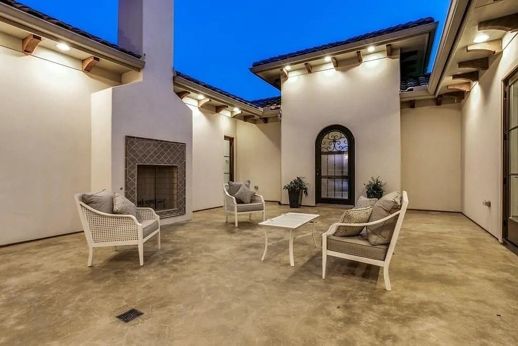 Outdoor patio with white furniture, a central fireplace, and surrounding arched windows.