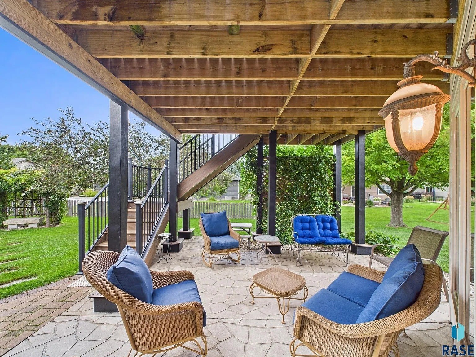 Covered patio with wicker furniture, blue cushions, and a view of a green garden.