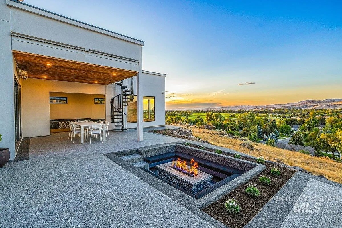 Modern patio with a fire pit, dining area, and scenic sunset view over a landscape.