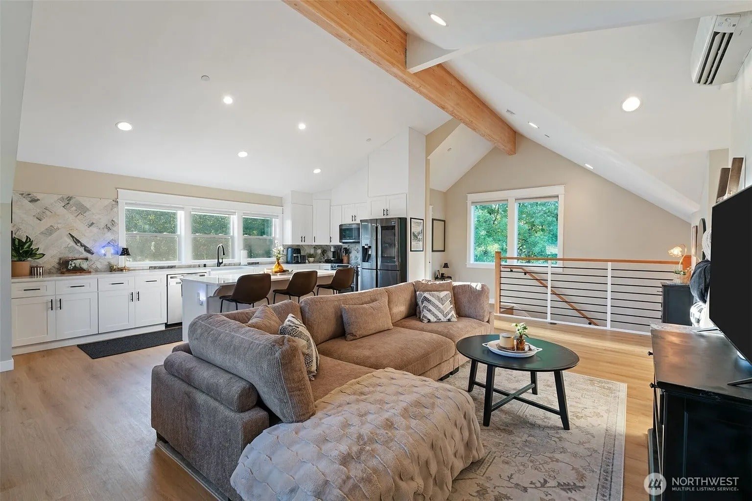 Modern open-concept living room and kitchen with wooden beams, cozy sectional sofa, and large windows.