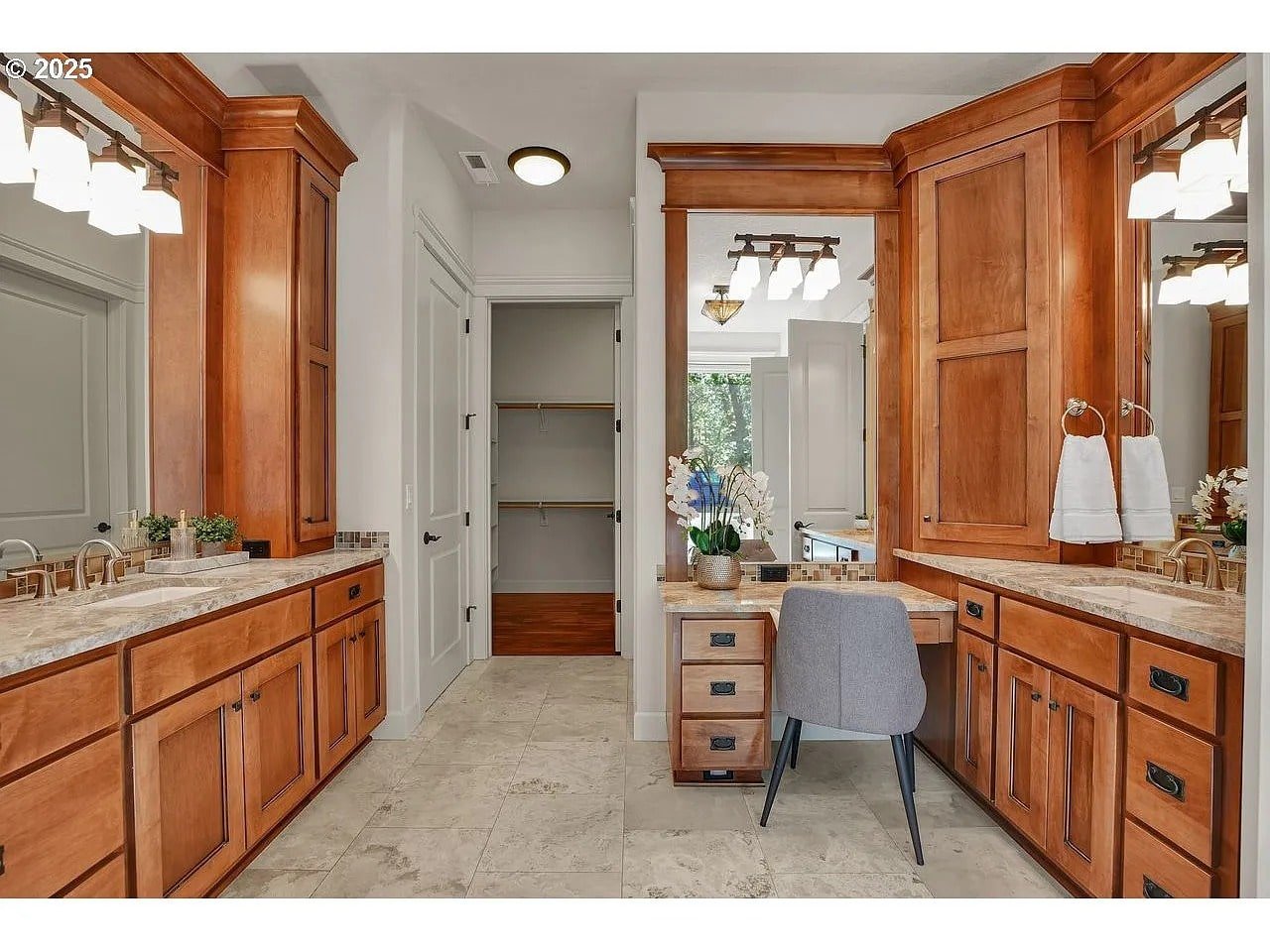 Spacious bathroom with wooden cabinets, marble countertops, dual sinks, and a vanity area with a chair.