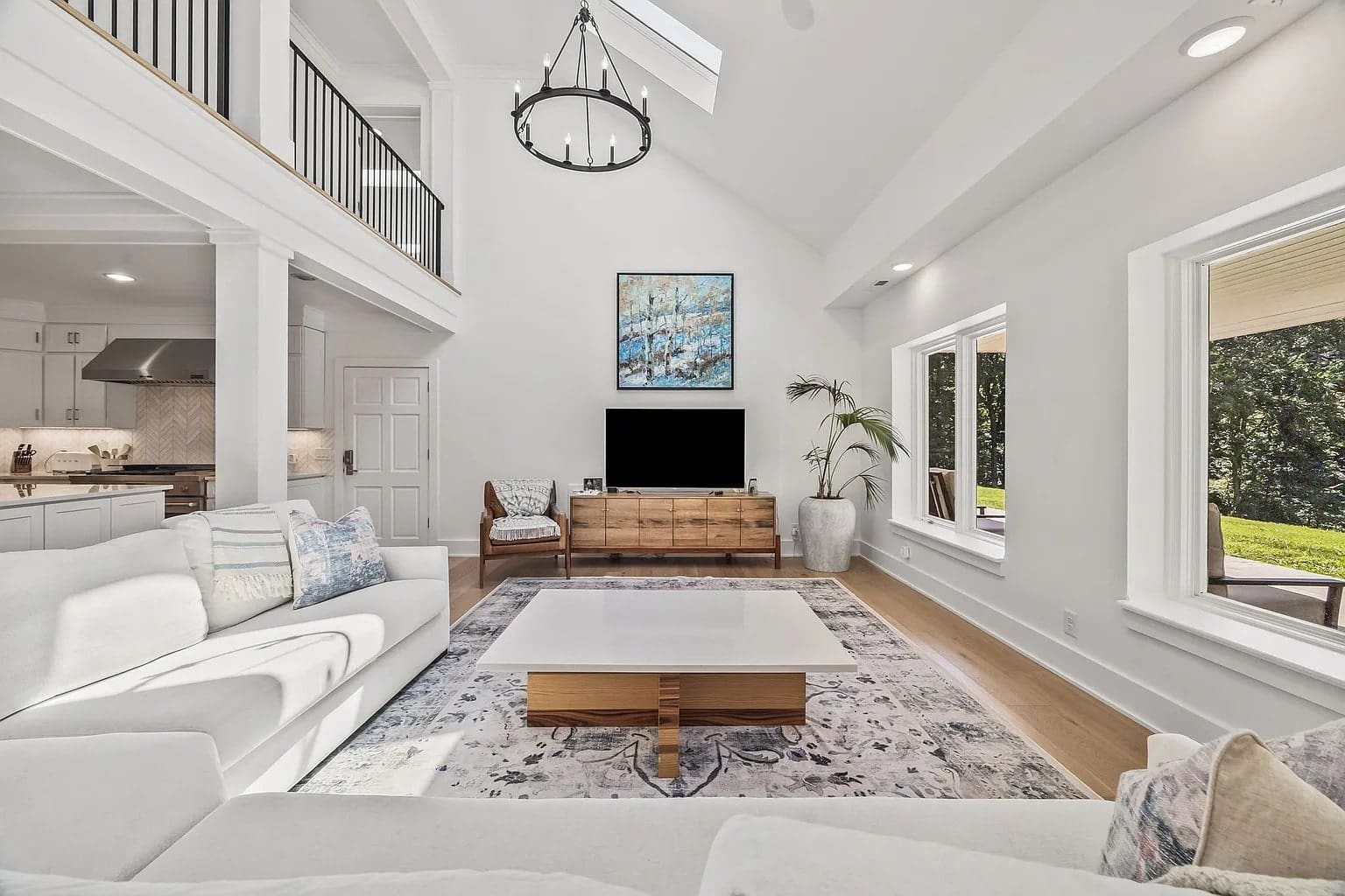 Spacious, bright living room with high ceilings, modern decor, and large windows overlooking greenery.