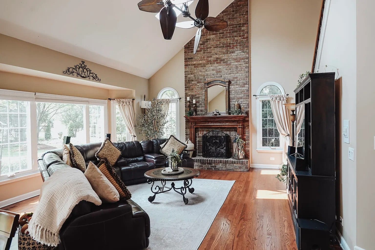Spacious living room with high ceiling, brick fireplace, leather sofas, and large windows.