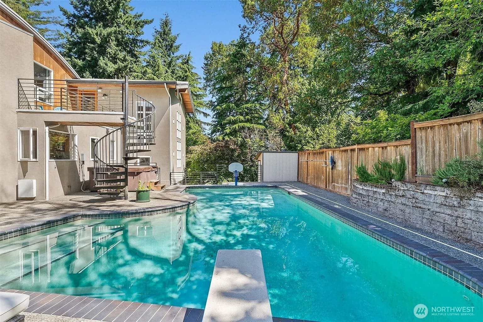 Backyard with a swimming pool, diving board, spiral staircase, and surrounding trees.