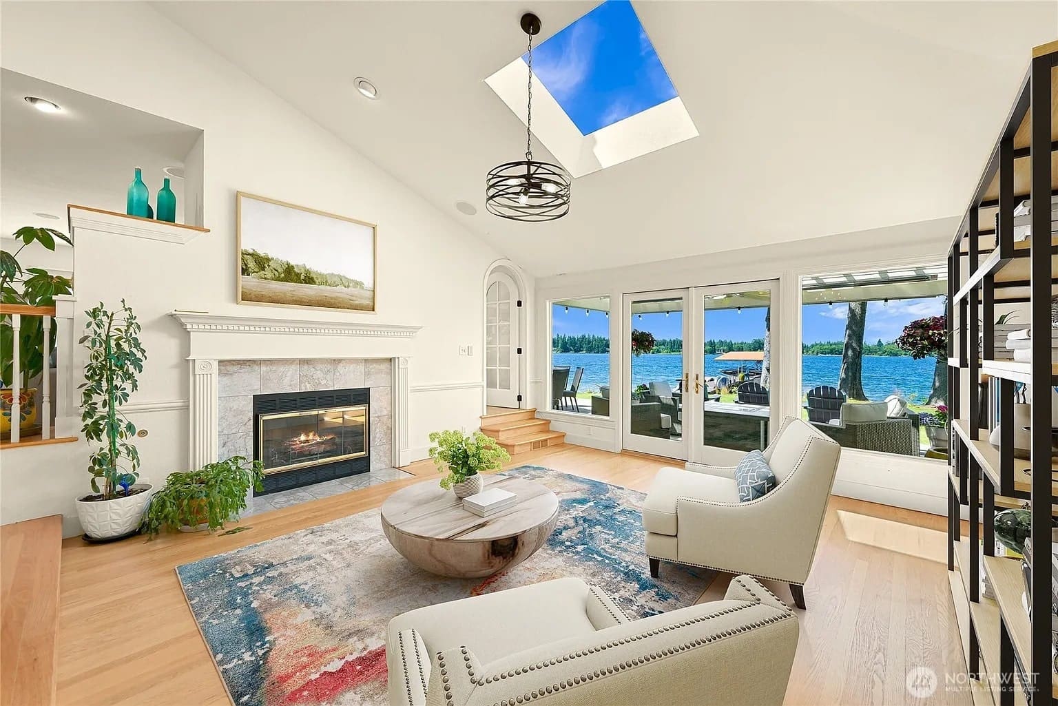 Bright living room with fireplace, skylight, and large windows overlooking a lake.