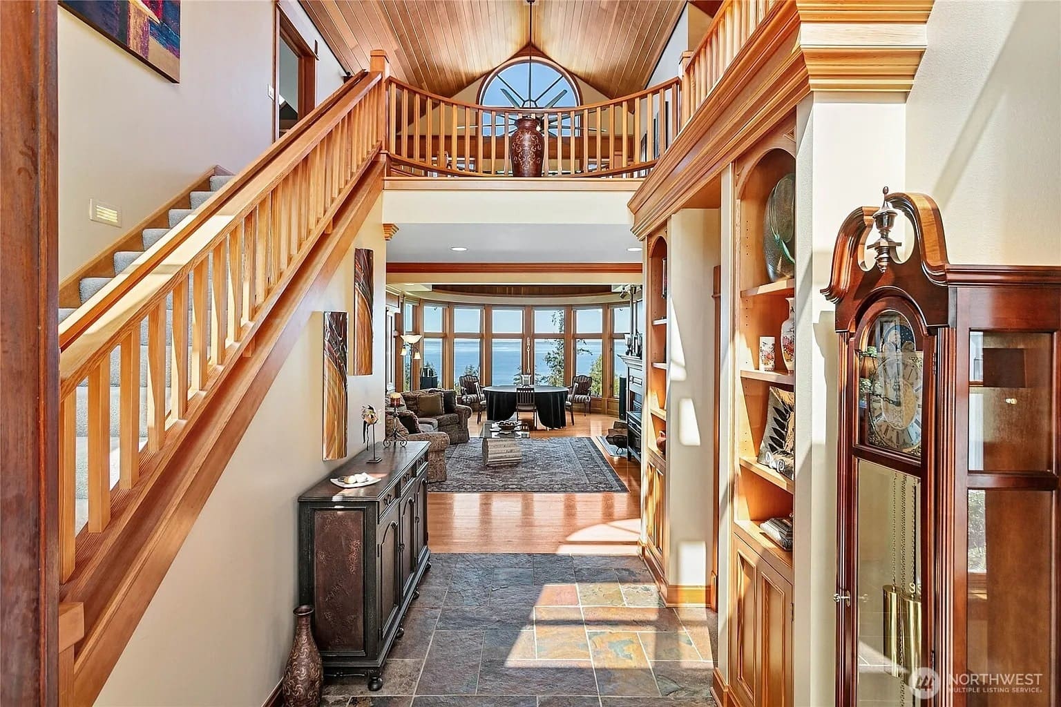 Spacious, sunlit foyer with wooden accents, leading to a living area with large windows.