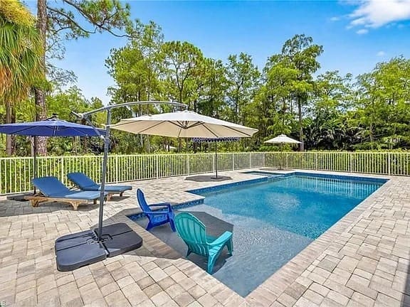 Outdoor pool area with lounge chairs, umbrellas, and surrounding trees.