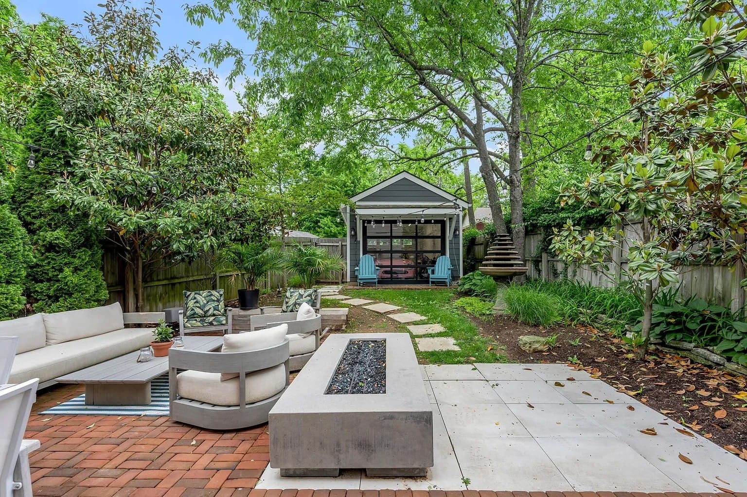 Backyard with patio furniture, fire pit, and a small shed surrounded by trees and greenery.