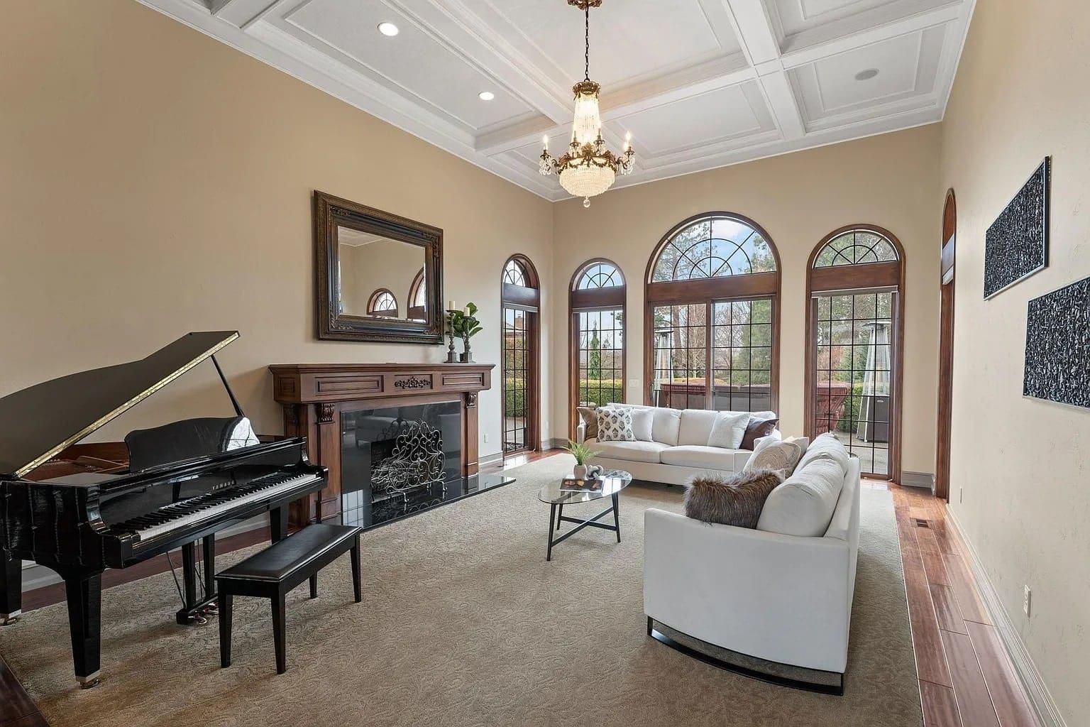 Elegant living room with a grand piano, fireplace, chandelier, and large arched windows.