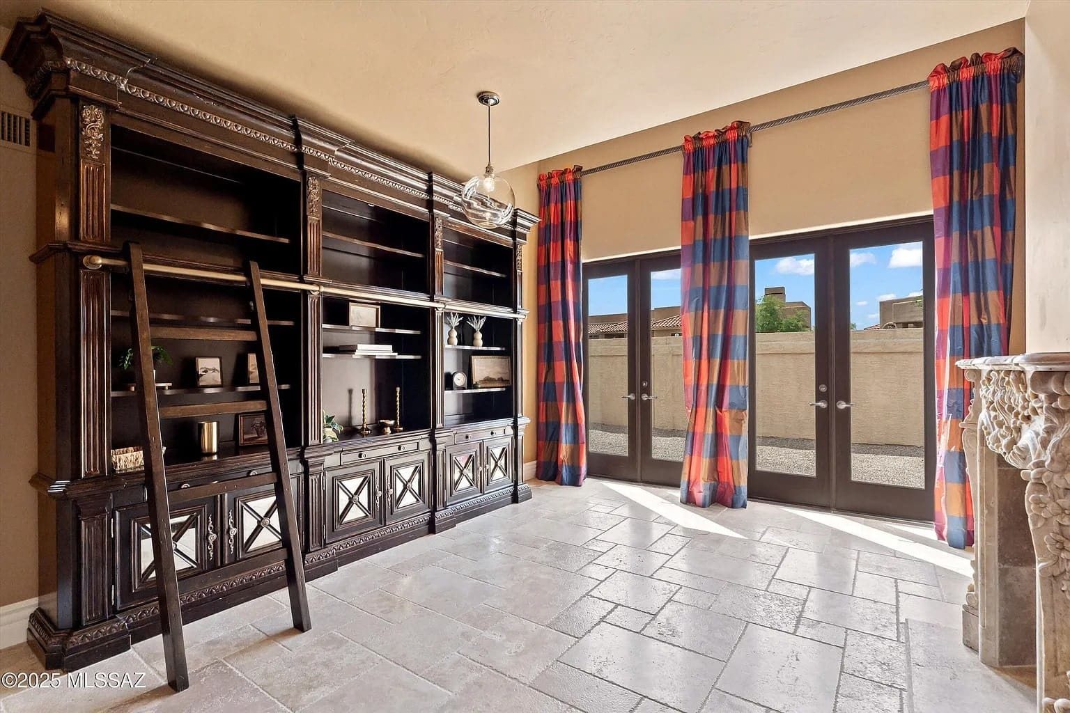 Room with large wooden bookshelf, ladder, and glass doors with red and blue curtains.