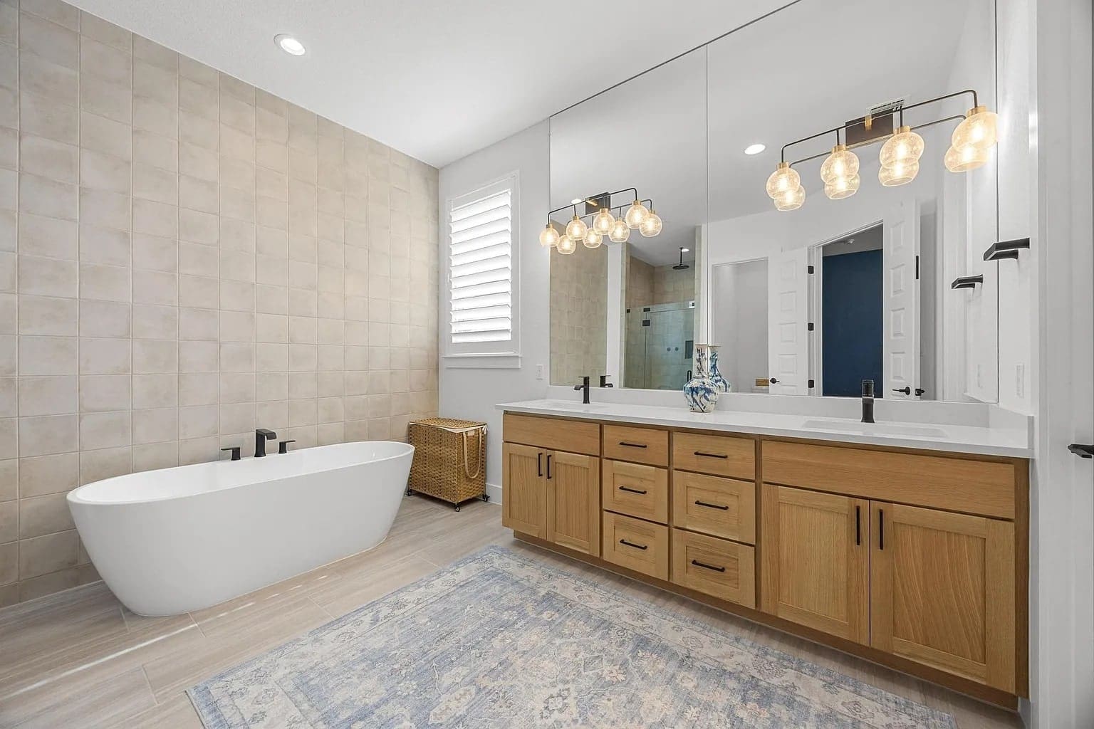Modern bathroom with freestanding tub, wooden vanity, large mirror, and decorative lighting.