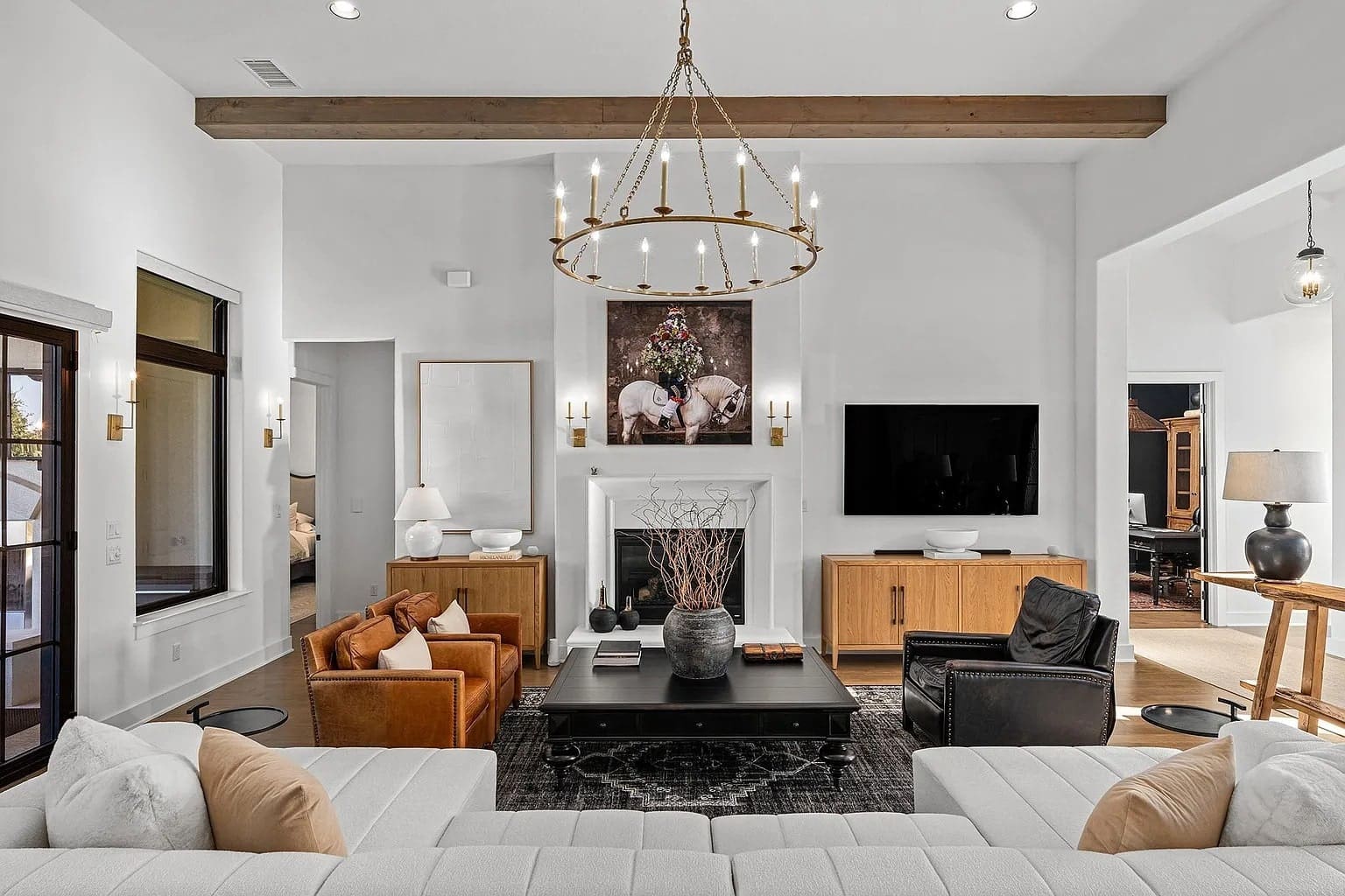 Modern living room with a chandelier, fireplace, large TV, and stylish furniture in neutral tones.