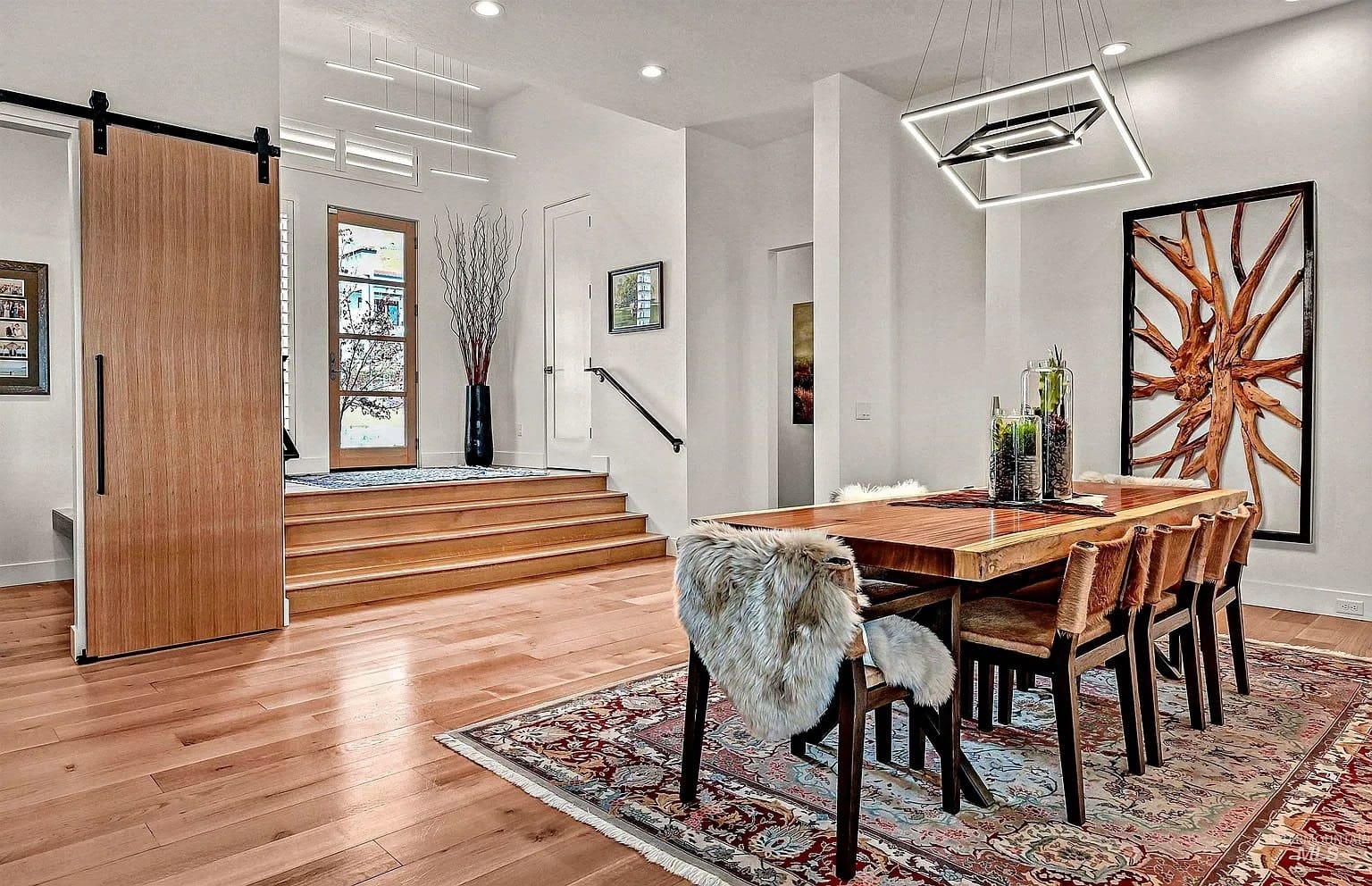 Modern dining room with wooden table, fur-covered chairs, geometric light fixture, and decorative wall art.