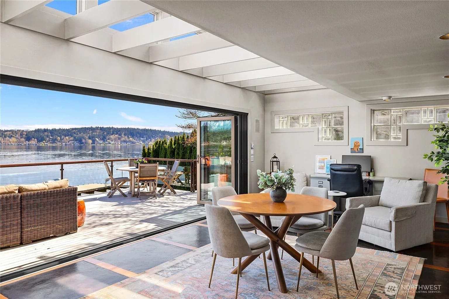 Modern living room with round table, chairs, and open sliding doors to a lakeside deck.