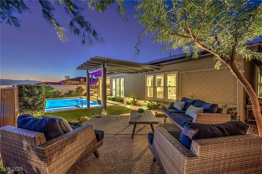 Outdoor patio with wicker furniture, overlooking a pool and garden, under a twilight sky.
