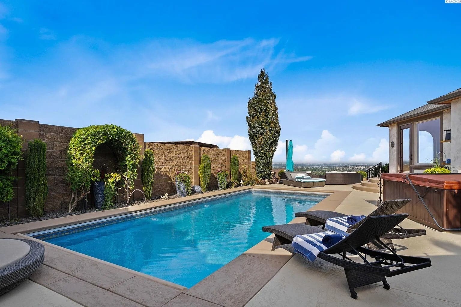 Outdoor pool area with lounge chairs, hot tub, and scenic view under a clear blue sky.