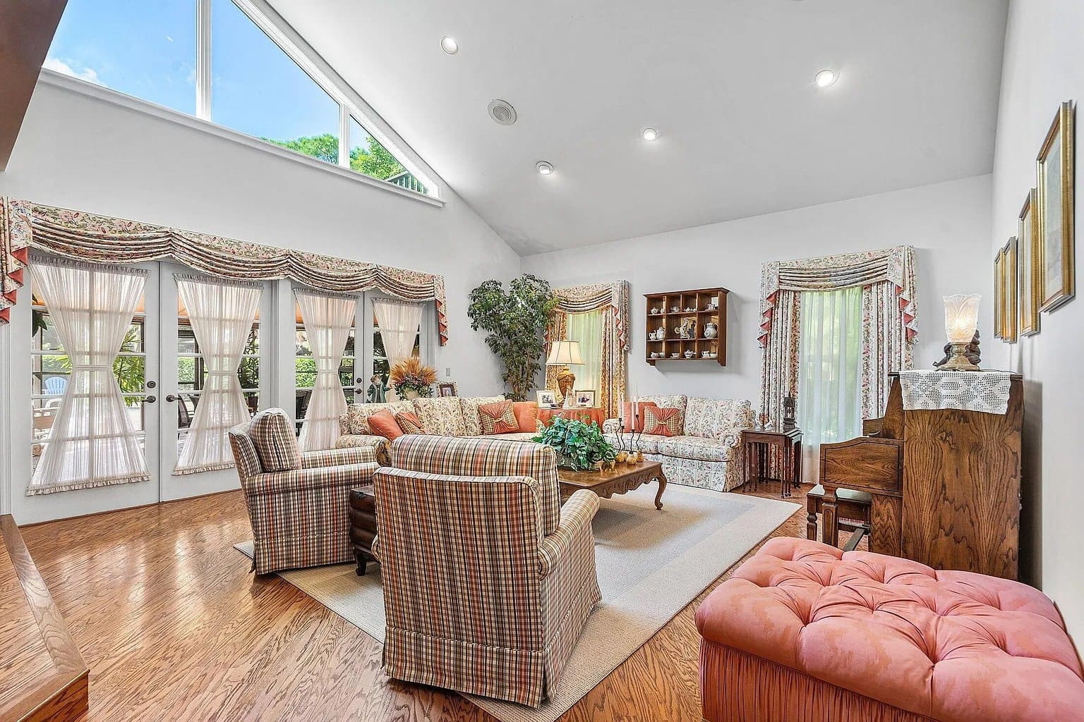 Spacious living room with large windows, patterned furniture, wooden floor, and decorative curtains.