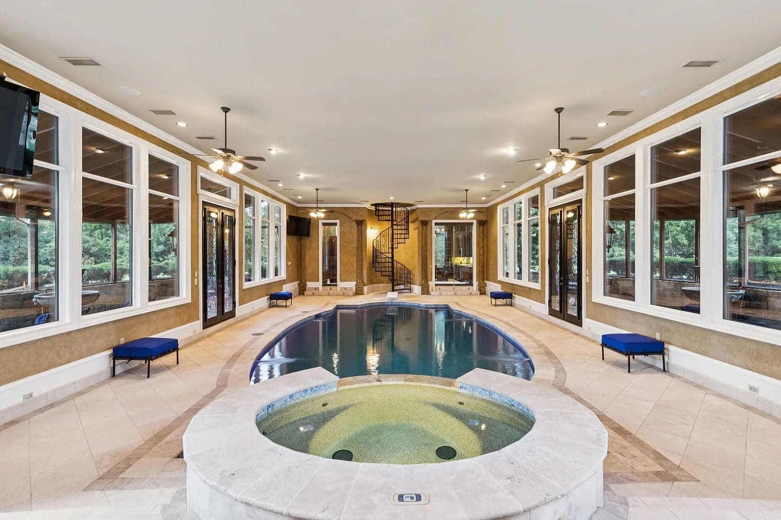 Indoor pool area with a central pool, surrounding windows, and a spiral staircase in the background.