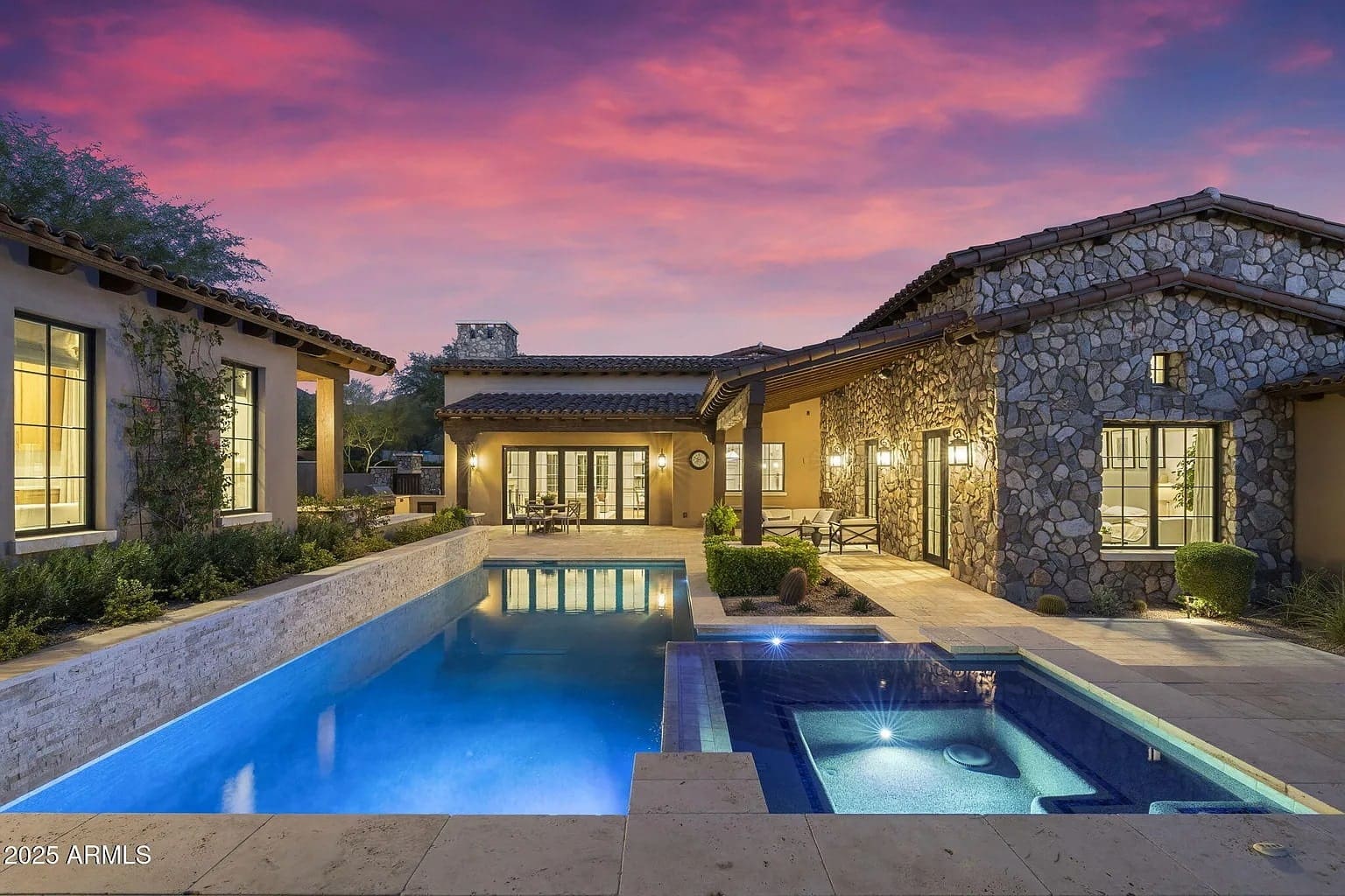 Luxury home with stone exterior, illuminated pool, and spa at sunset.