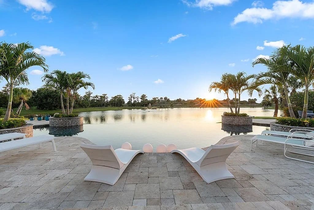 Two lounge chairs by a serene pool with palm trees and a sunset view.