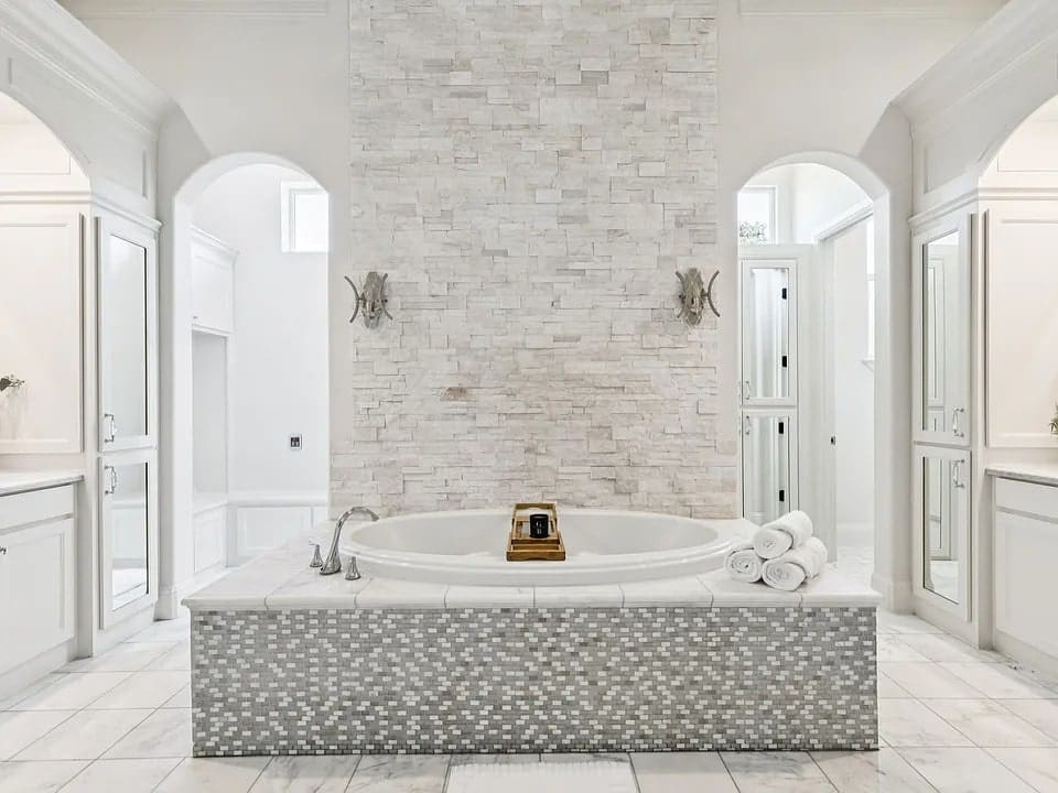 Luxurious bathroom with a central bathtub, stone accent wall, and elegant white decor.