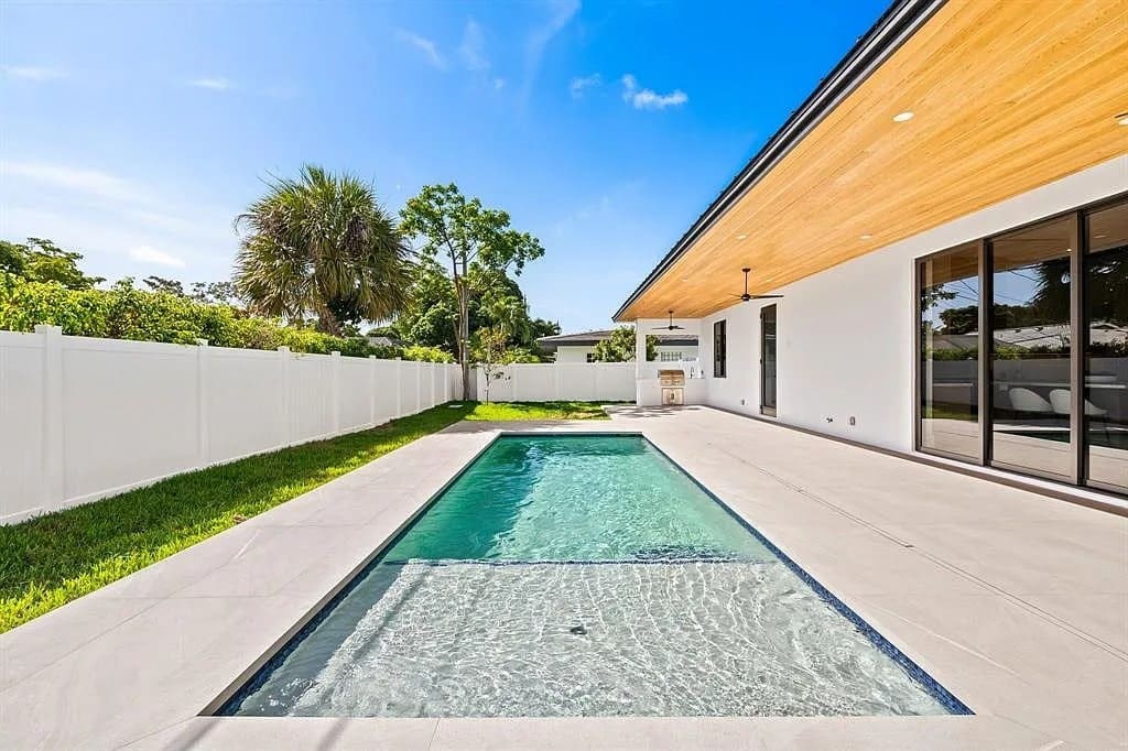 Modern backyard with a rectangular swimming pool, white fence, and a wooden patio ceiling.