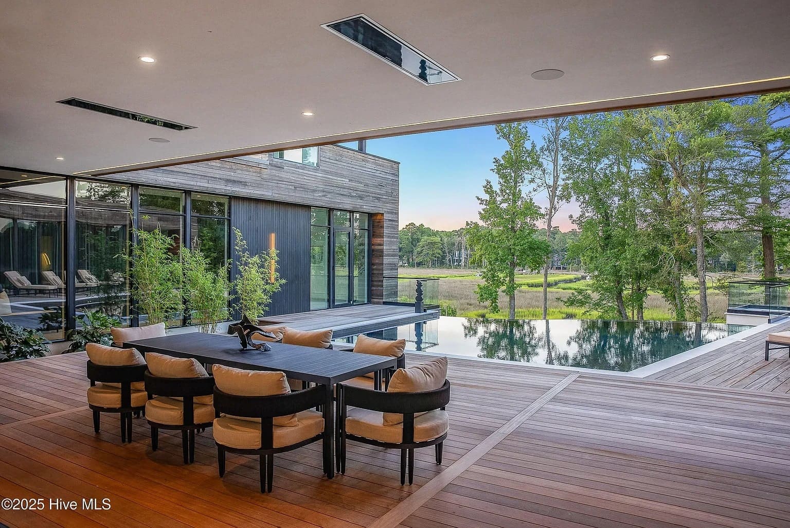 Modern outdoor patio with dining table, overlooking an infinity pool and scenic wooded landscape.