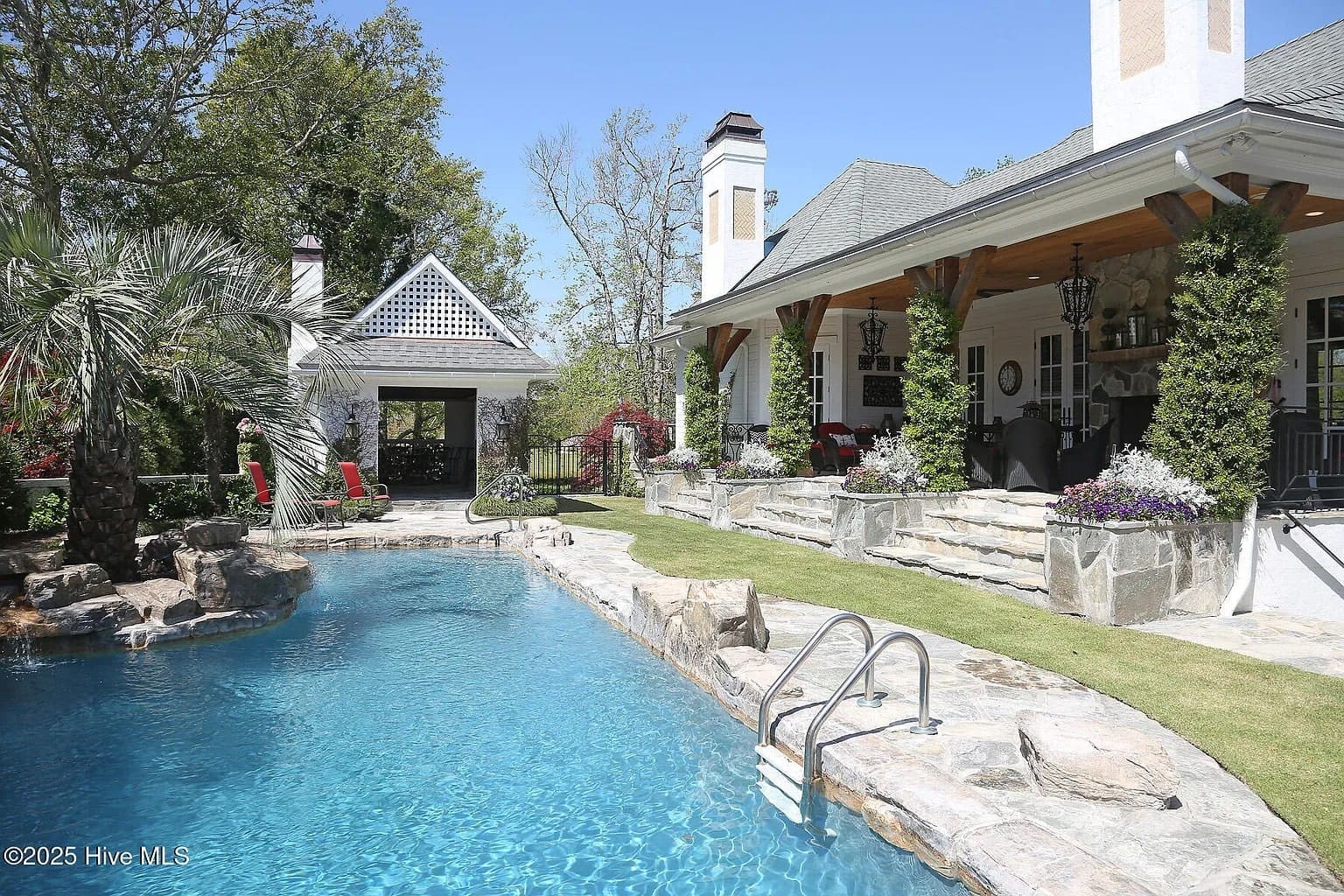 Luxurious backyard with a swimming pool, stone patio, and a covered porch with seating.