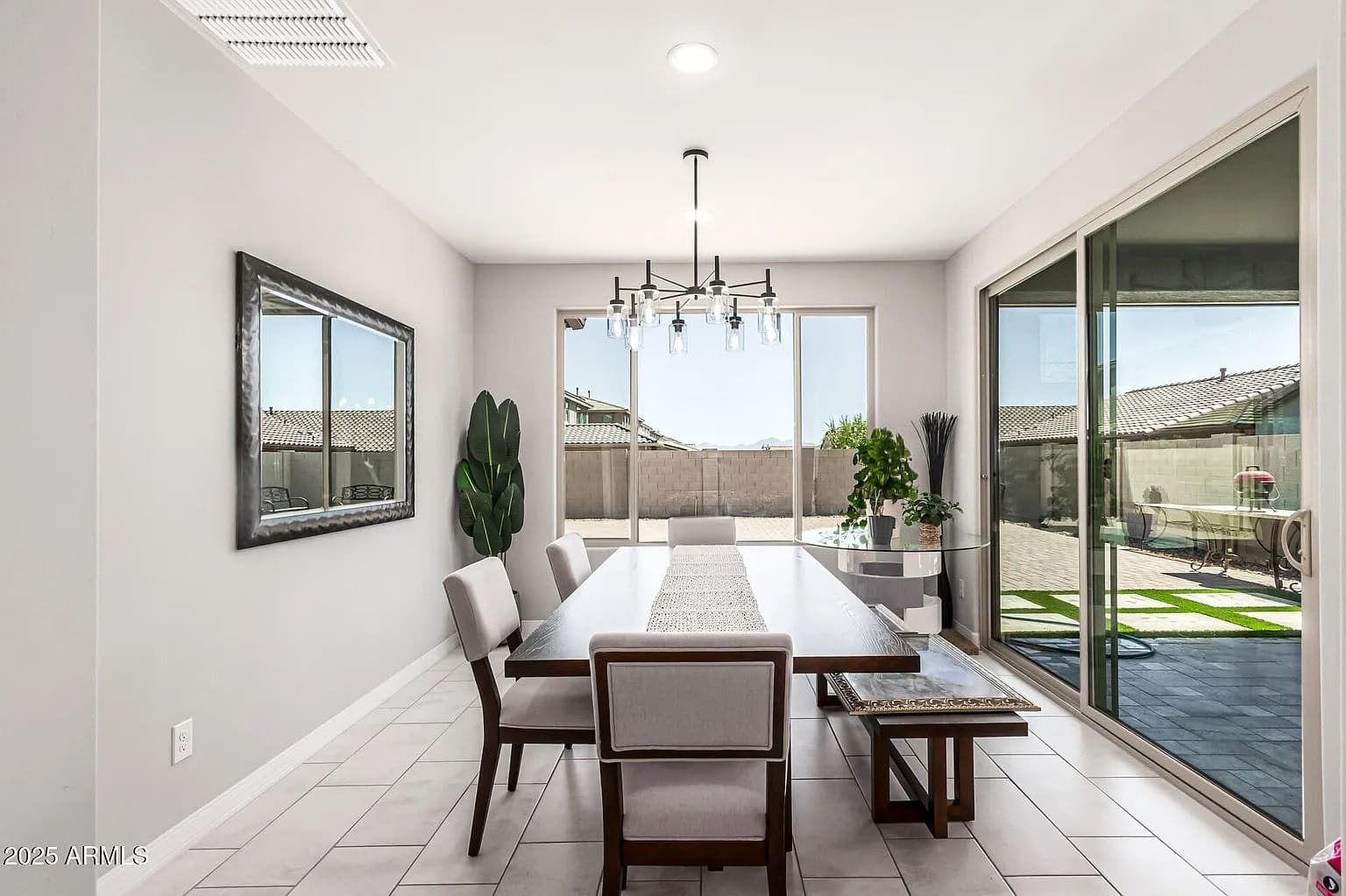 Modern dining room with a large table, chairs, chandelier, and sliding glass doors to a patio.