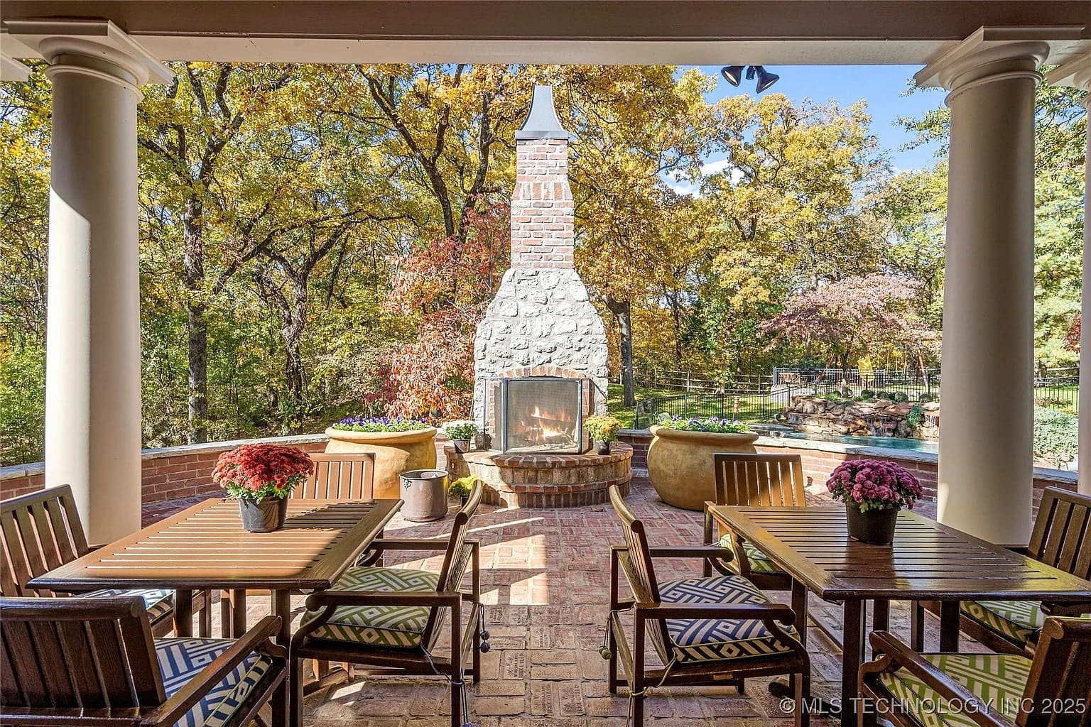 Outdoor patio with a stone fireplace, wooden dining set, and surrounding autumn trees.