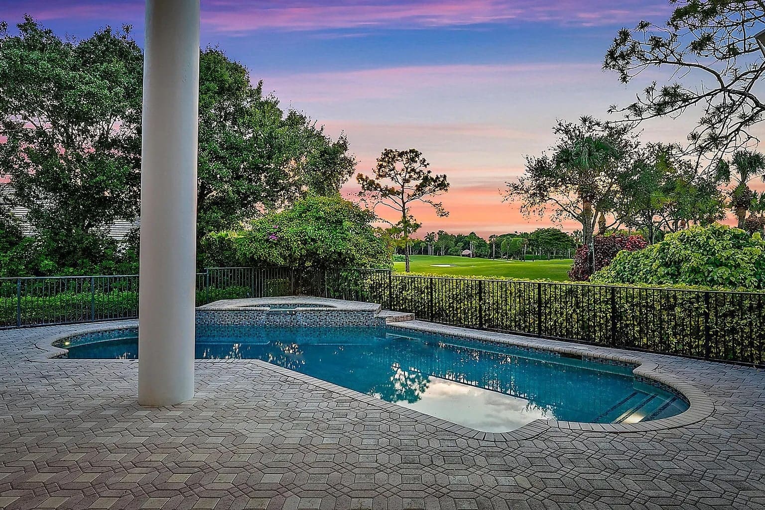 Backyard pool with surrounding greenery and a sunset sky in the background.
