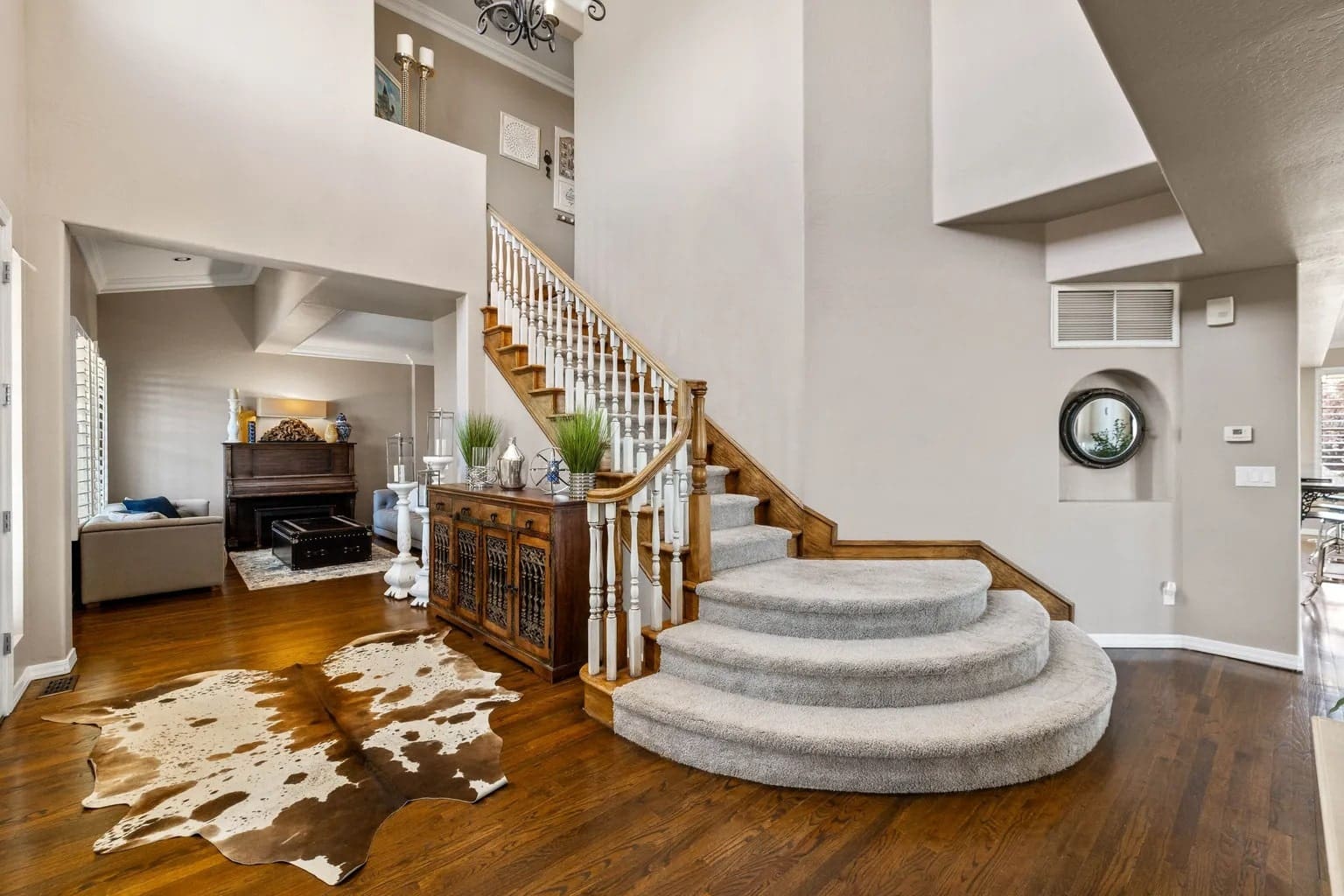 Spacious foyer with curved carpeted staircase, wooden floors, and a cowhide rug.
