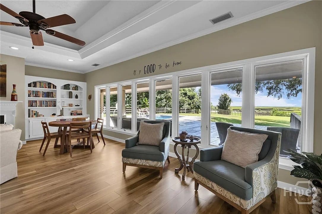 Spacious living room with large windows, pool view, wooden floor, and cozy seating area.