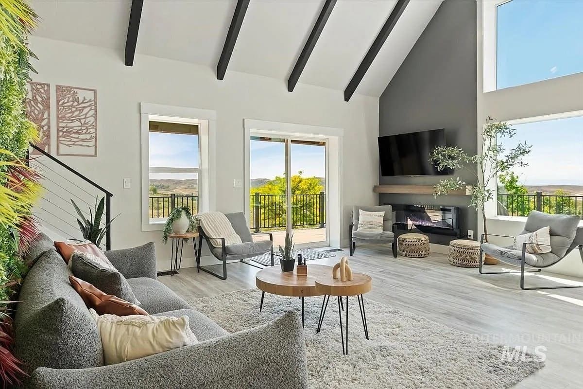 Modern living room with vaulted ceiling, large windows, gray sofa, and a wall-mounted TV.
