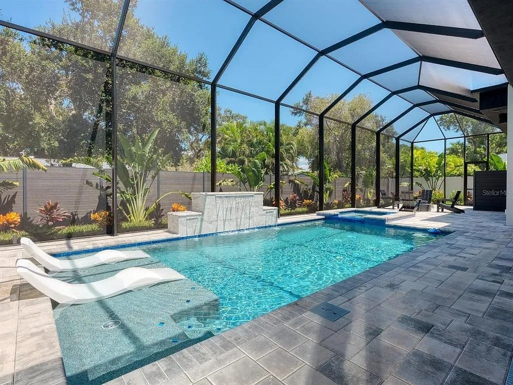 Enclosed outdoor pool area with lounge chairs, waterfall feature, and surrounding tropical plants.

