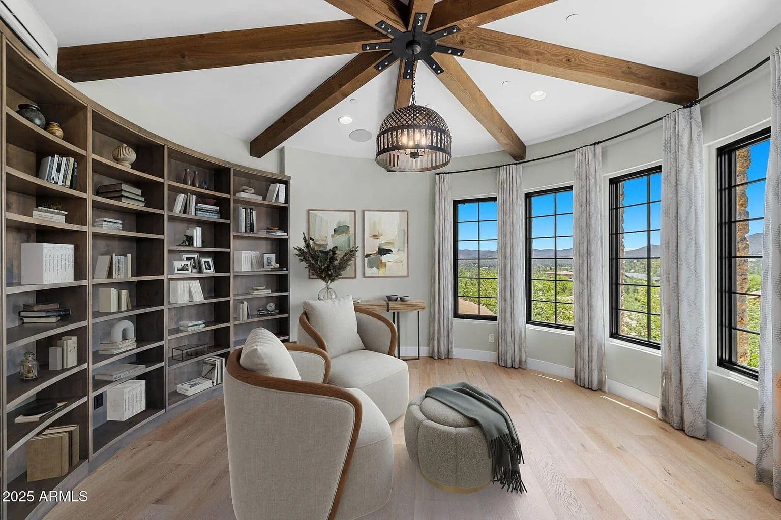 Cozy reading nook with armchairs, bookshelves, large windows, and wooden ceiling beams.