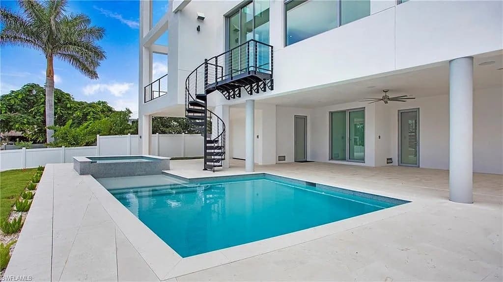 Modern house exterior with a spiral staircase, pool, and patio area under a clear sky.