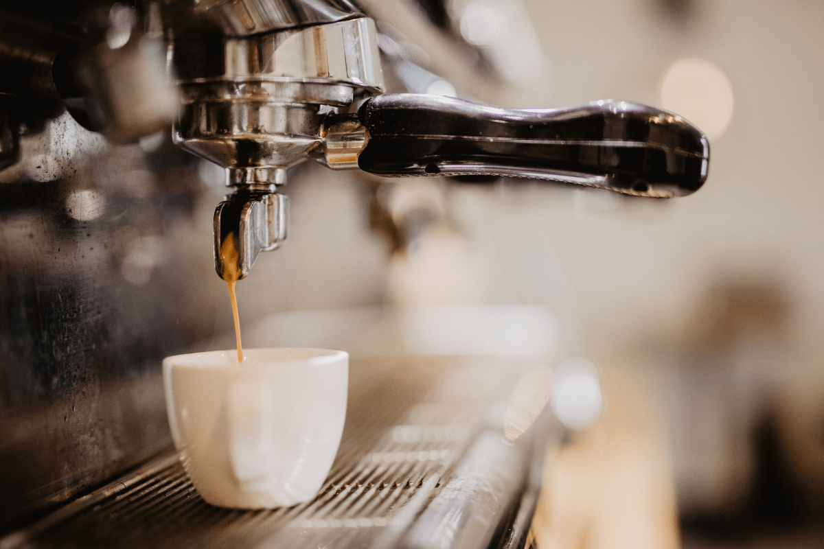 A close-up of an espresso machine pouring coffee into a white cup, with a warm, blurred background creating a cozy atmosphere.