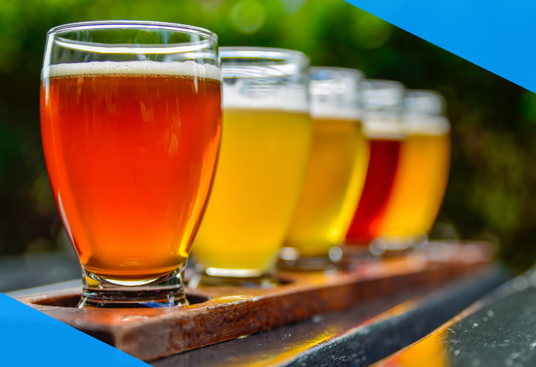 A flight of four different beers in glasses on a wooden tray.