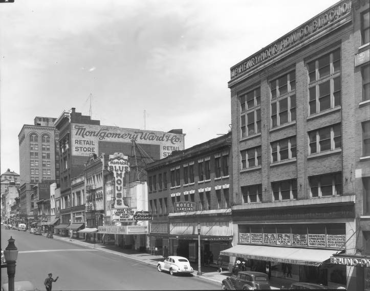 Historic city street with Montgomery Ward retail store, vintage cars, and 1940s-era buildings.