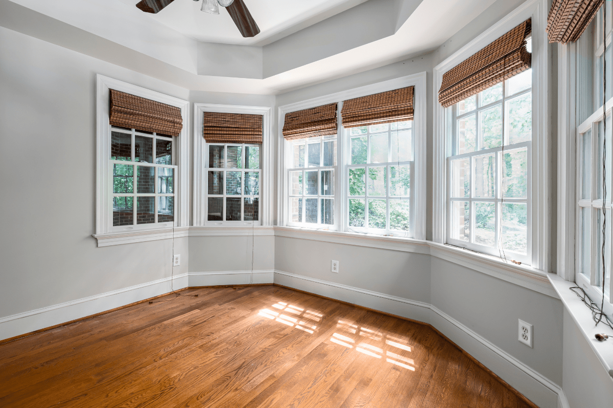 Energy-Efficient-Home-Upgrades-min A bright, empty room with hardwood floors features a bay window with five sections, each adorned with brown woven blinds, allowing sunlight to stream in and illuminate the space.