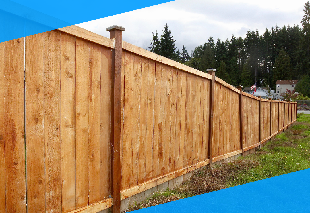 Wooden fence stretching across a grassy area with trees and a house in the background.