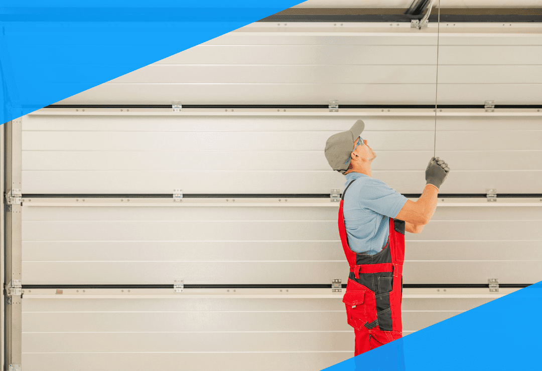 Worker in red overalls adjusting a garage door mechanism inside a garage.