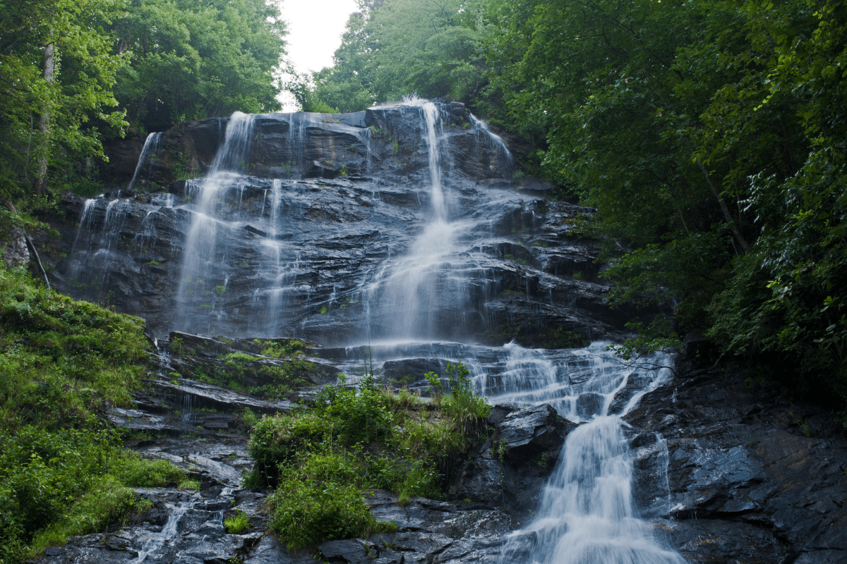 A cascading waterfall flows down a rocky cliff surrounded by lush green trees and vegetation.