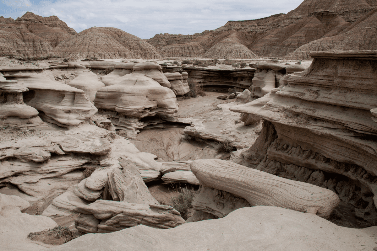 A rugged desert landscape featuring eroded rock formations and layered sedimentary structures under a cloudy sky.