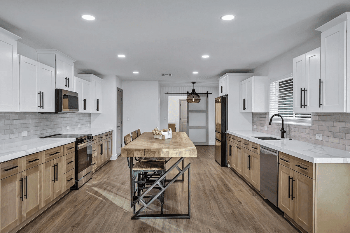 Spacious modern kitchen with wooden island, white cabinets, stainless steel appliances, and wood flooring.
